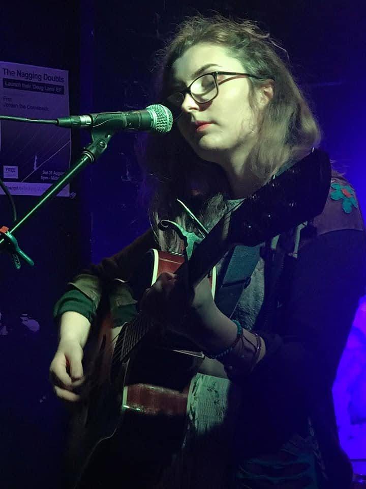 Aimée singing with eyes closed under blue stage light
