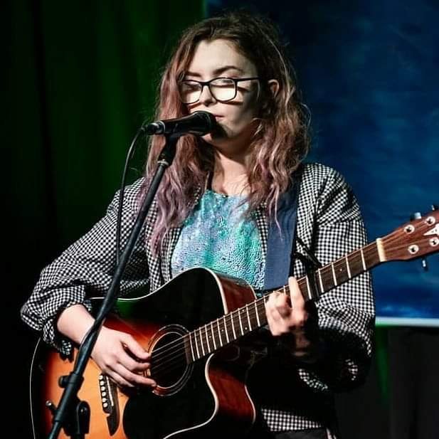 Close-up of Aimée singing with pink-toned hair and glasses