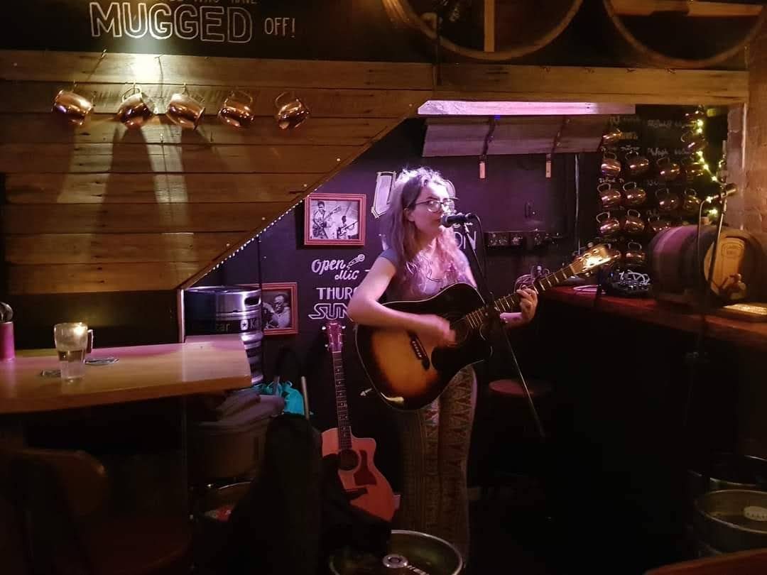Aimée at an open-mic night surrounded by copper and wood